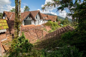 A traditional house with a steeply pitched roof, surrounded by lush greenery and mountains in the background.