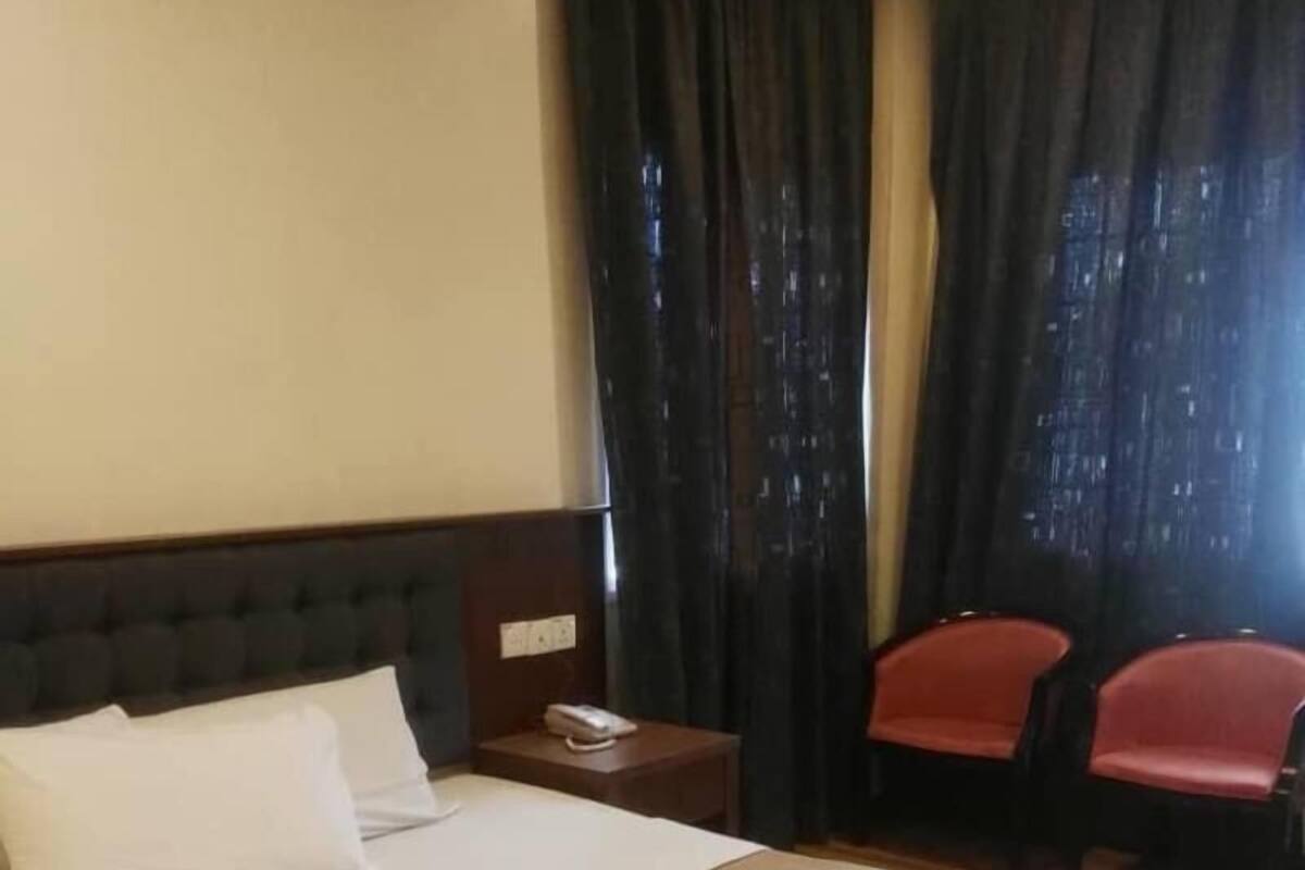 Een hotelkamer met een groot bed, een nachtkastje met een telefoon, een stoel en een raam met gordijnen.