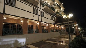 A multi-story building with balconies, a tiled walkway, and street lamps.