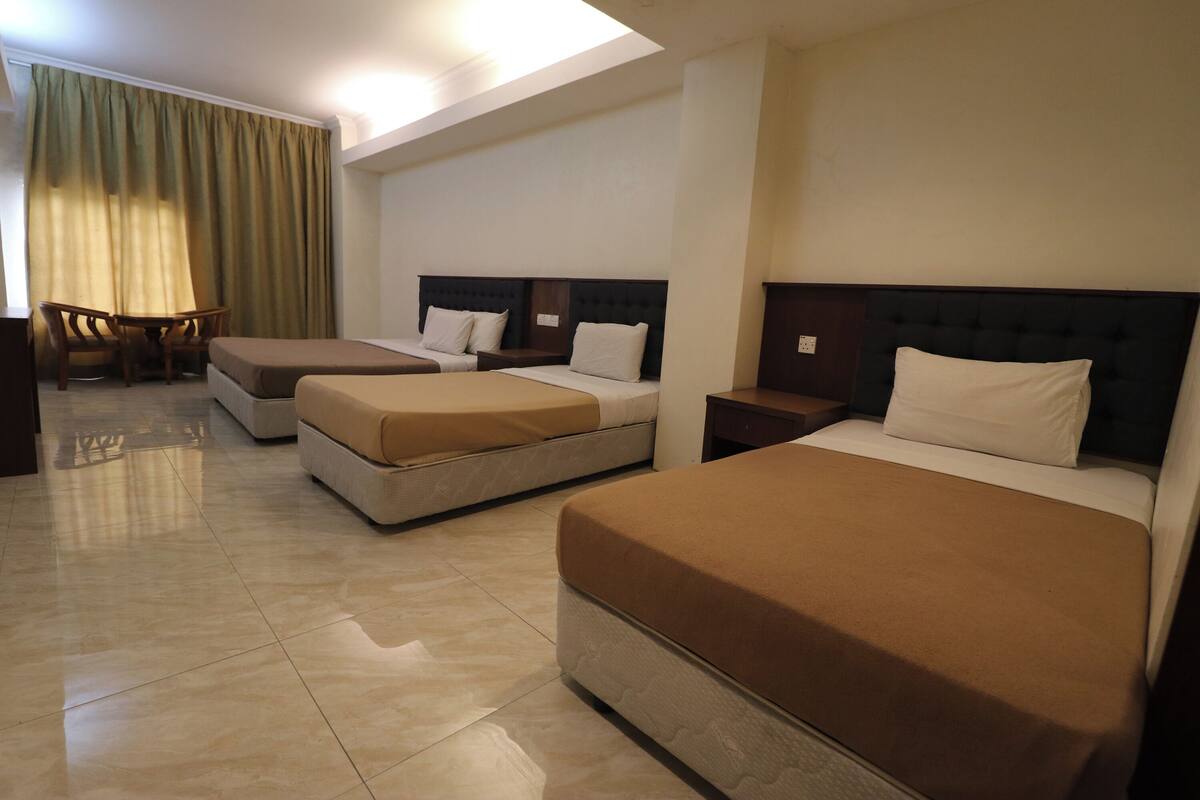 Een hotelkamer met drie bedden, een bureau en een stoel.