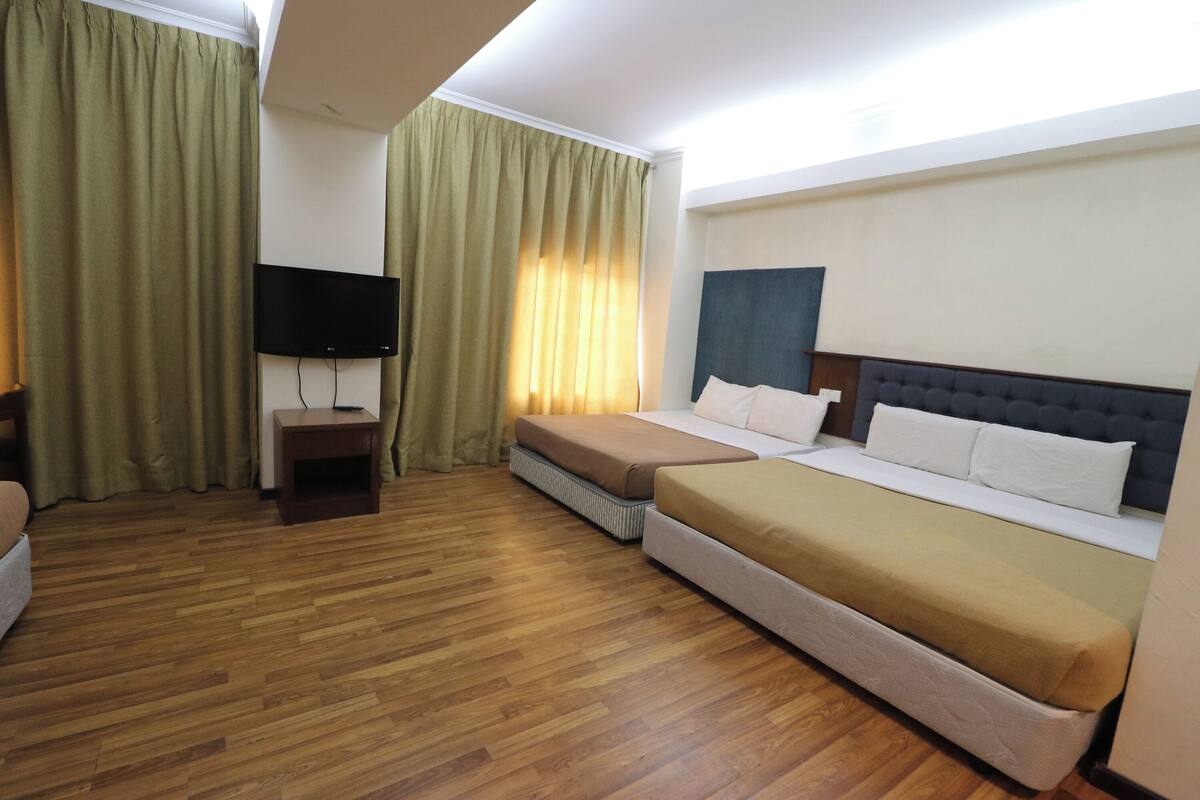 Een hotelkamer met twee bedden, een televisie op een standaard en een houten vloer.