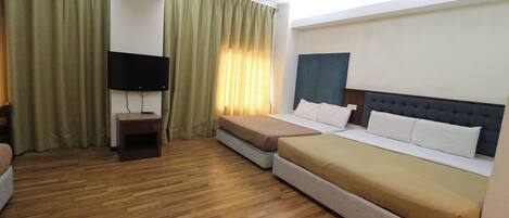 Quarto de hotel com duas camas, uma televisão sobre suporte e piso de madeira.