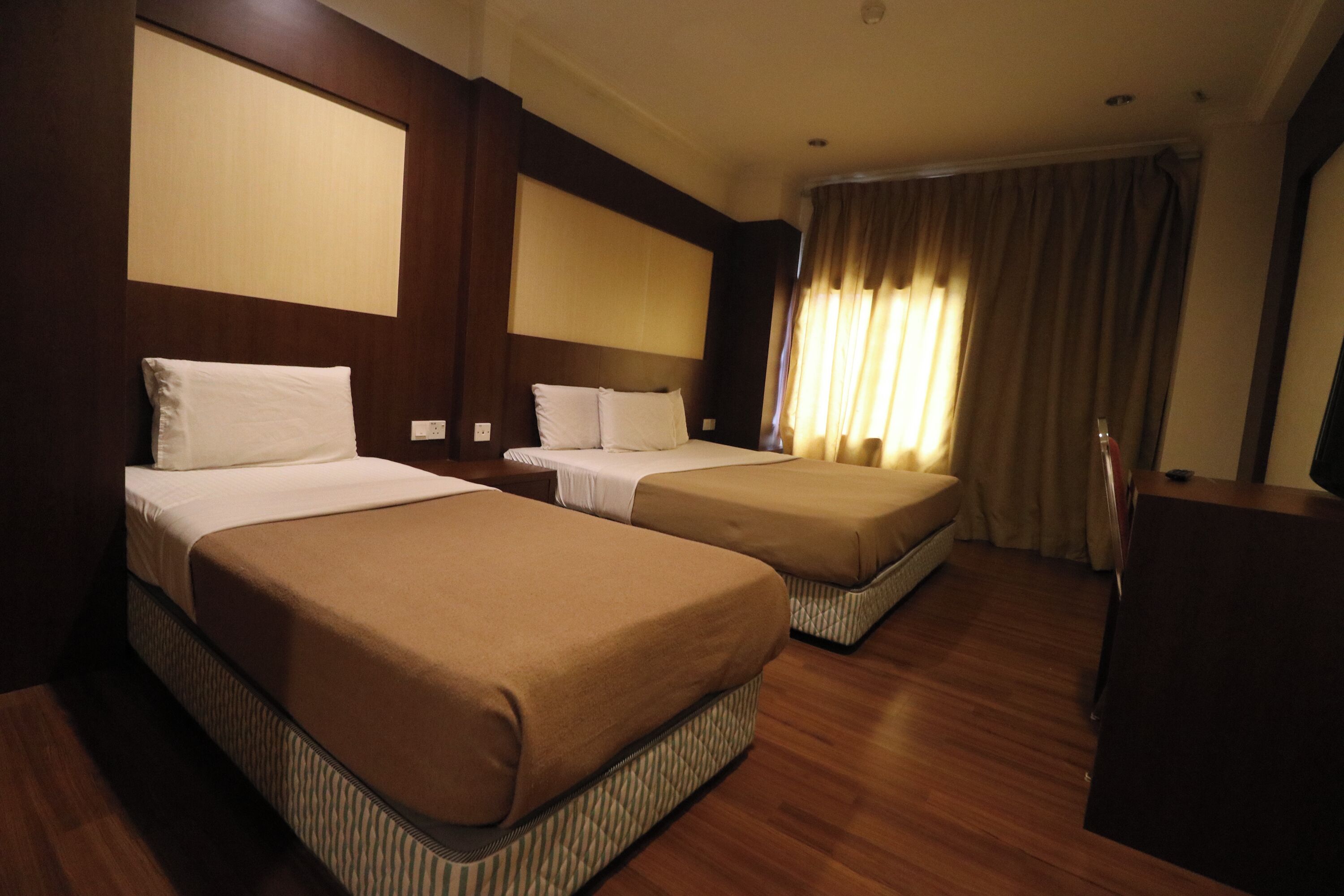 A hotel room with two beds, wooden flooring, and a large window with curtains.
