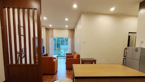 Een compacte hotelkamer met een houten vloer, een eettafel met vier stoelen, een bank, een klein tafeltje en een koelkast.