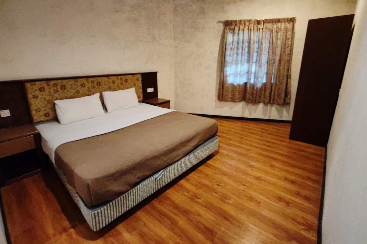 A bedroom with a wooden floor, a bed with a brown blanket, a nightstand, a window with curtains, and a wardrobe.