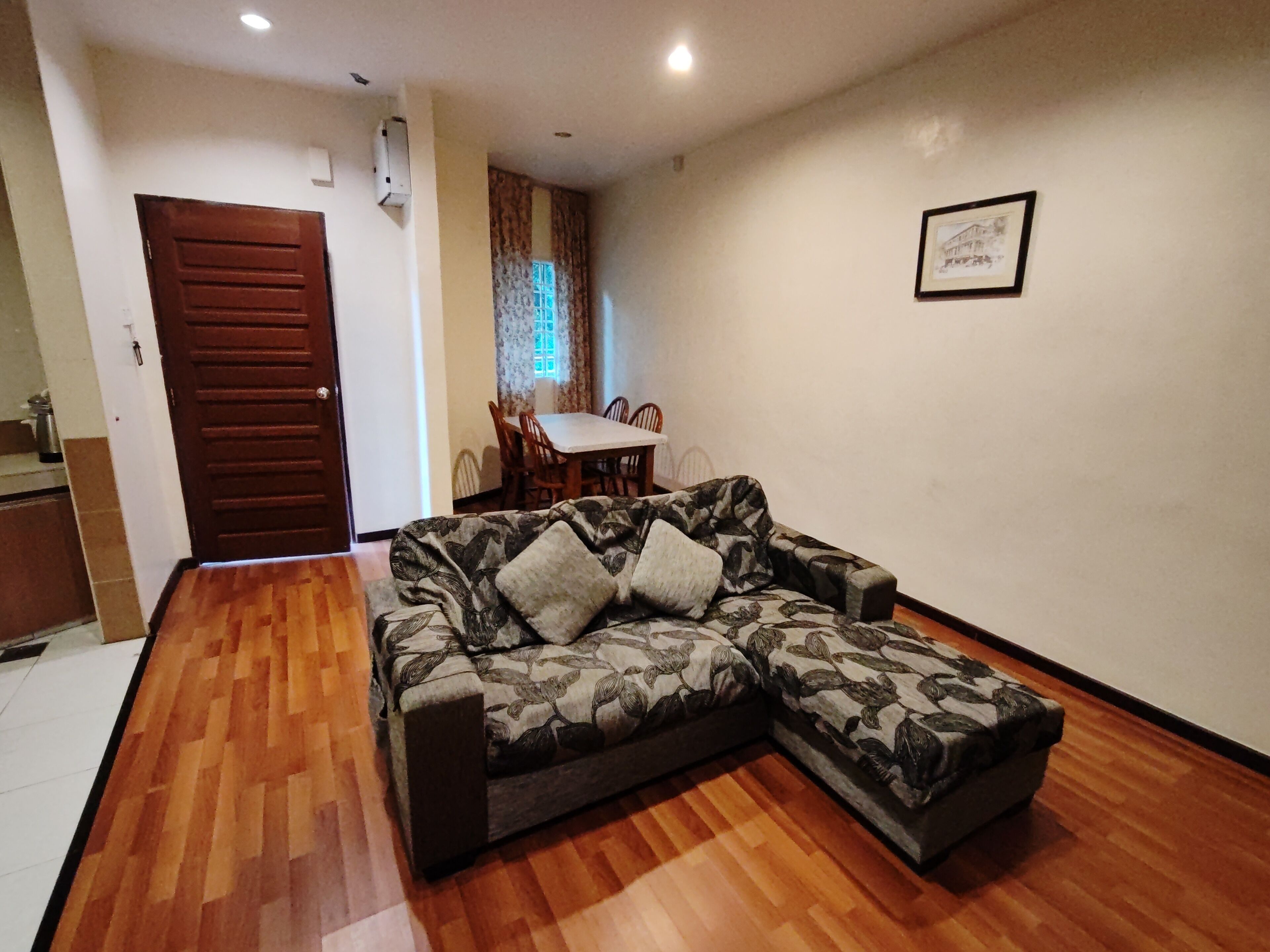 A living room with a sofa, wooden flooring, a dining area with chairs and a table, and a door.