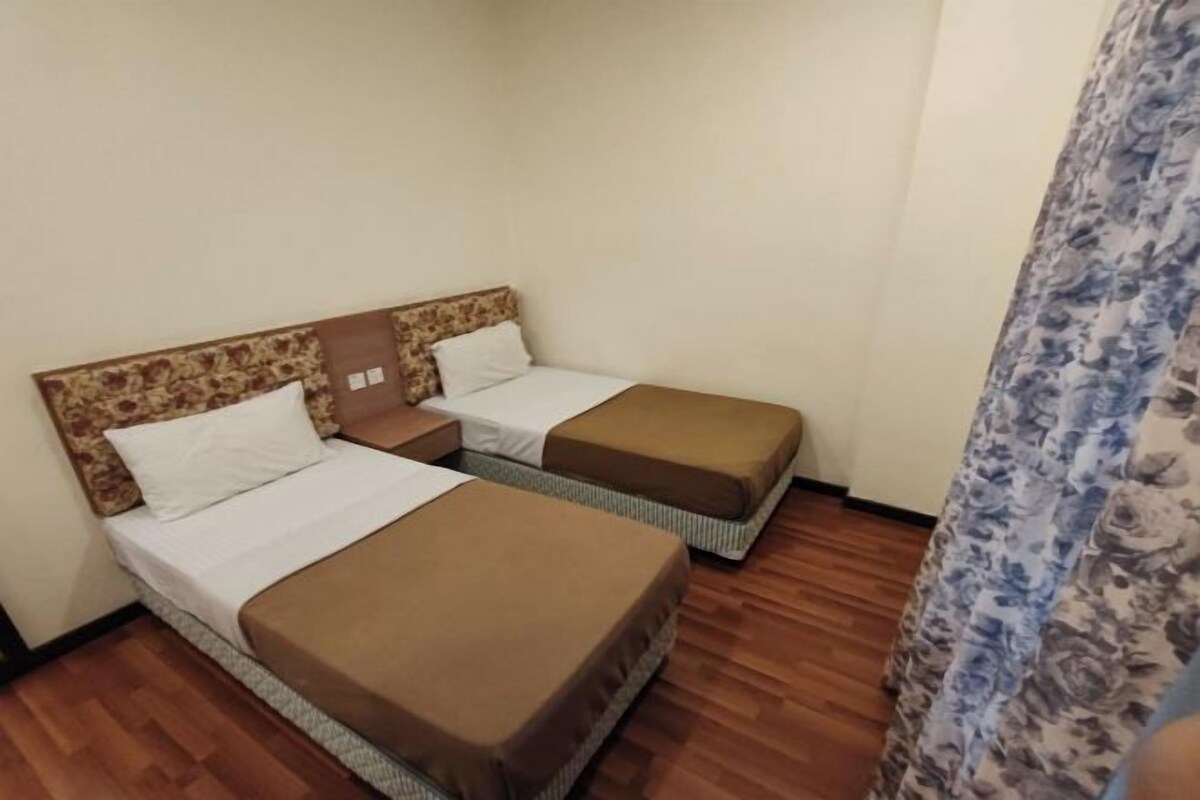 A hotel room with two single beds, wooden flooring, and a floral curtain.