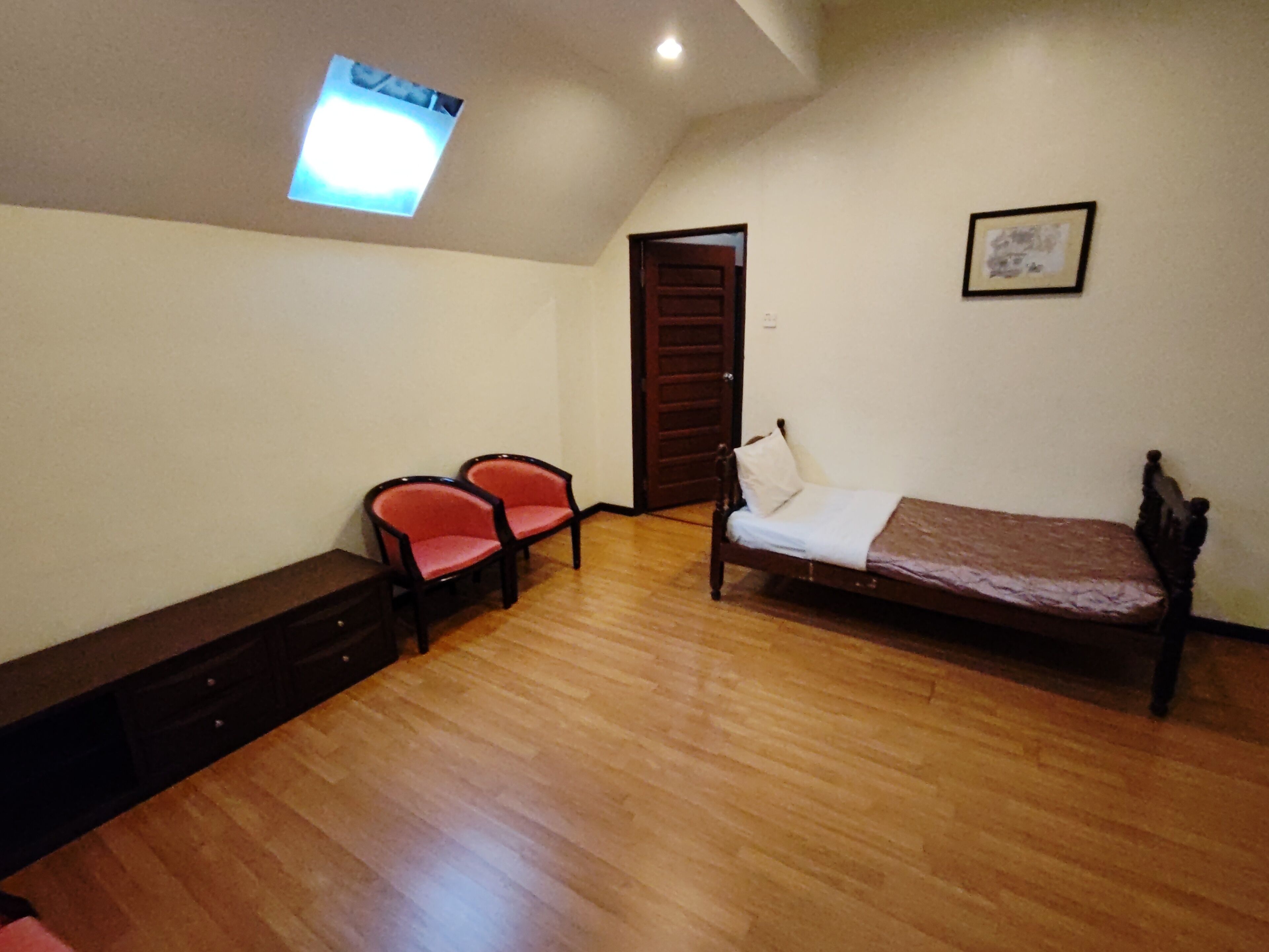 Een slaapkamer met houten vloer, een bed, twee stoelen, een kleintje tafel, een deur en een plafondlamp.