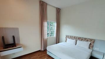 A hotel room with a bed, a TV on a stand, a window with curtains, and a wooden floor.