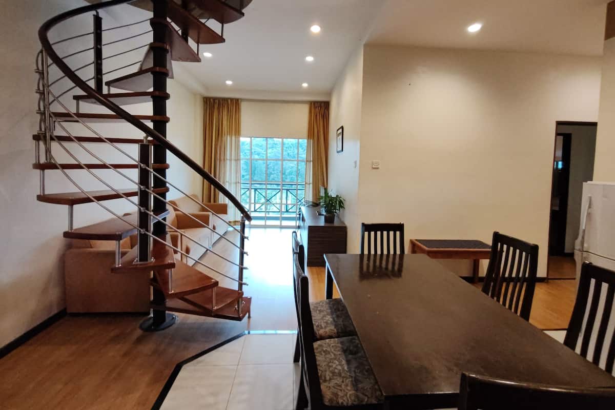 A spacious dining area with a long wooden table and chairs, a spiral staircase, and a large window with curtains.