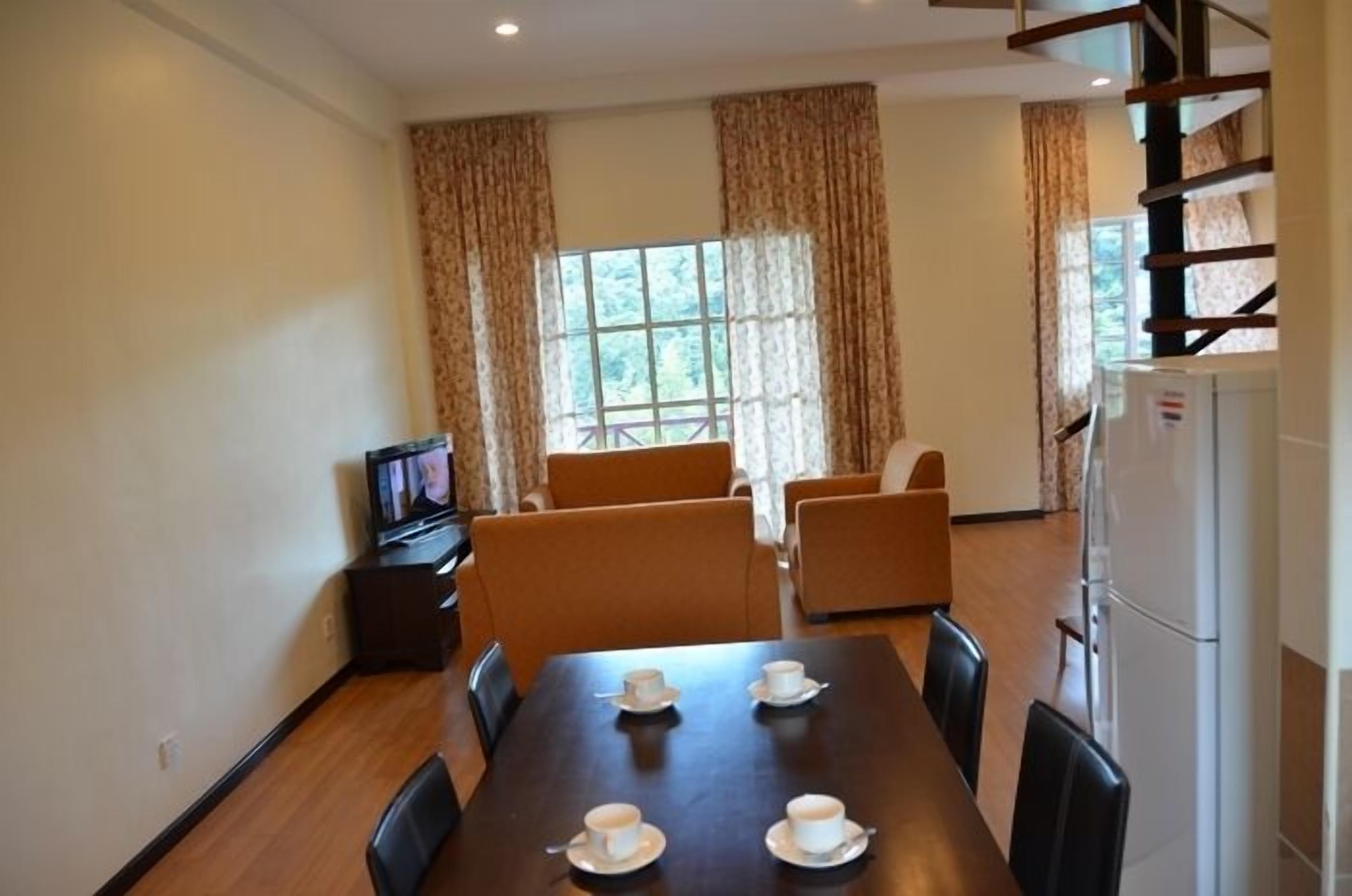 A dining area with a table set for four, a television on a stand, and a refrigerator.