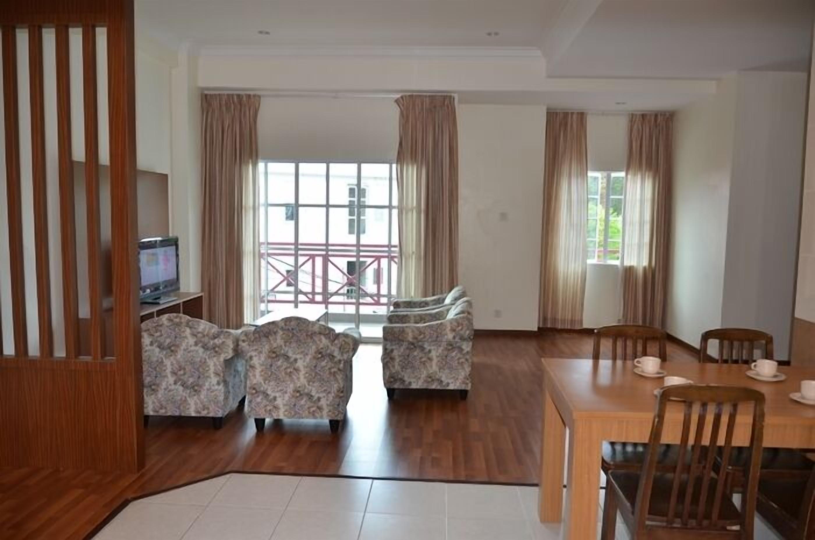 A spacious living area with a wooden dining table, floral-patterned sofas, and a TV on a stand.