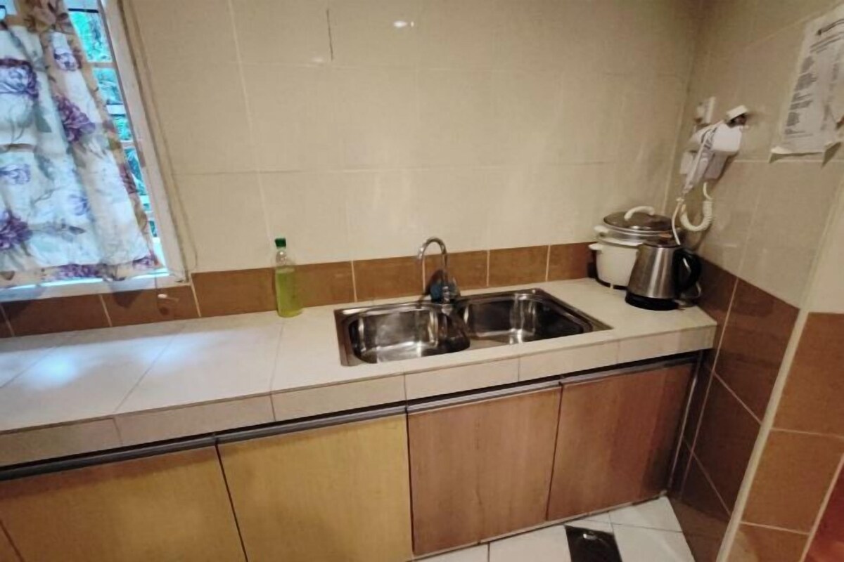 A compact kitchen with a stainless steel sink, a stove, and a small window with a floral curtain.