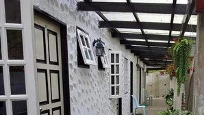 A covered outdoor corridor with a white textured wall, a door with a window, and a chair. - Hillview Inn (Tanah Rata)