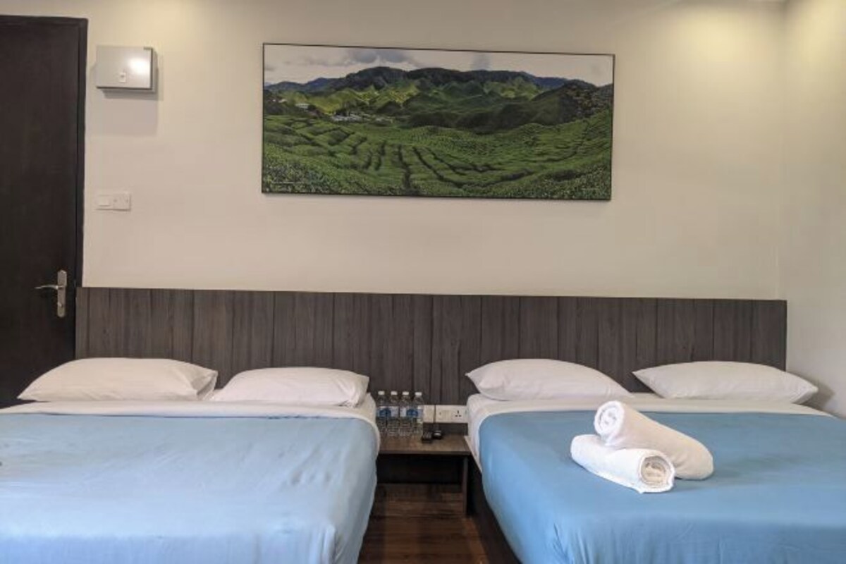A hotel room with two beds, a painting of a landscape, and a nightstand with toiletries.
