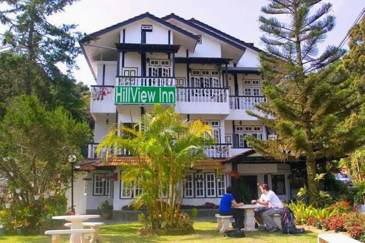 Un edificio de dos plantas con un cartel que dice 'Hillview Inn'. Hay mesas y sillas afuera, y una persona sentada en una de ellas.