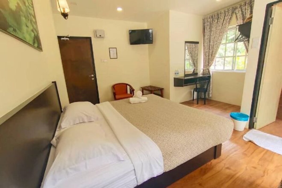 A bedroom with a bed, a desk, a chair, a TV, and a window with curtains.