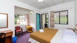 A hotel room with a bed, a desk, a chair, a small table, and a window with curtains. - Hillview Inn (Tanah Rata)
