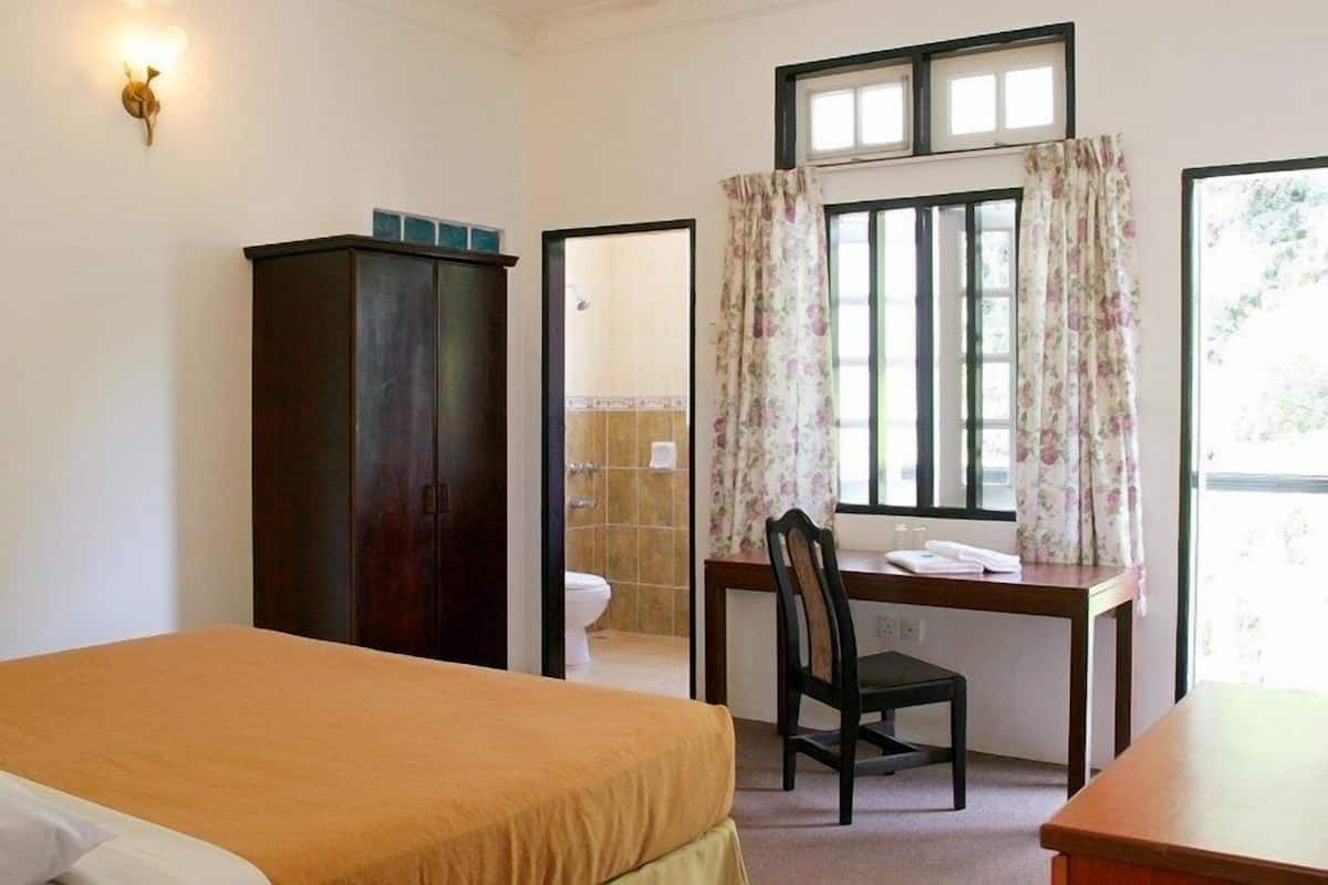 A bedroom with a bed, a desk, a chair, a wardrobe, and a window with curtains.