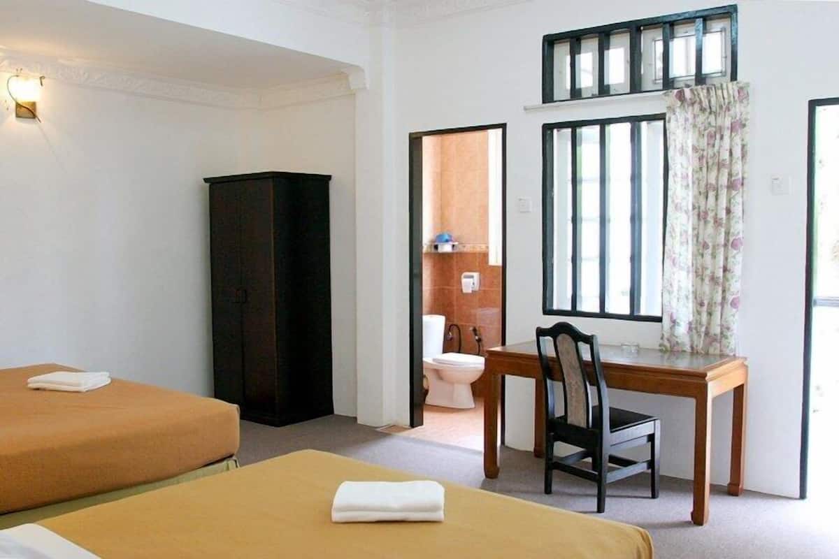 A hotel room with two beds, a wooden desk, a chair, a wardrobe, and a bathroom visible through an open door.