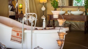 A bathroom with a bathtub, a sink, a mirror, and a bedside table with a lamp.