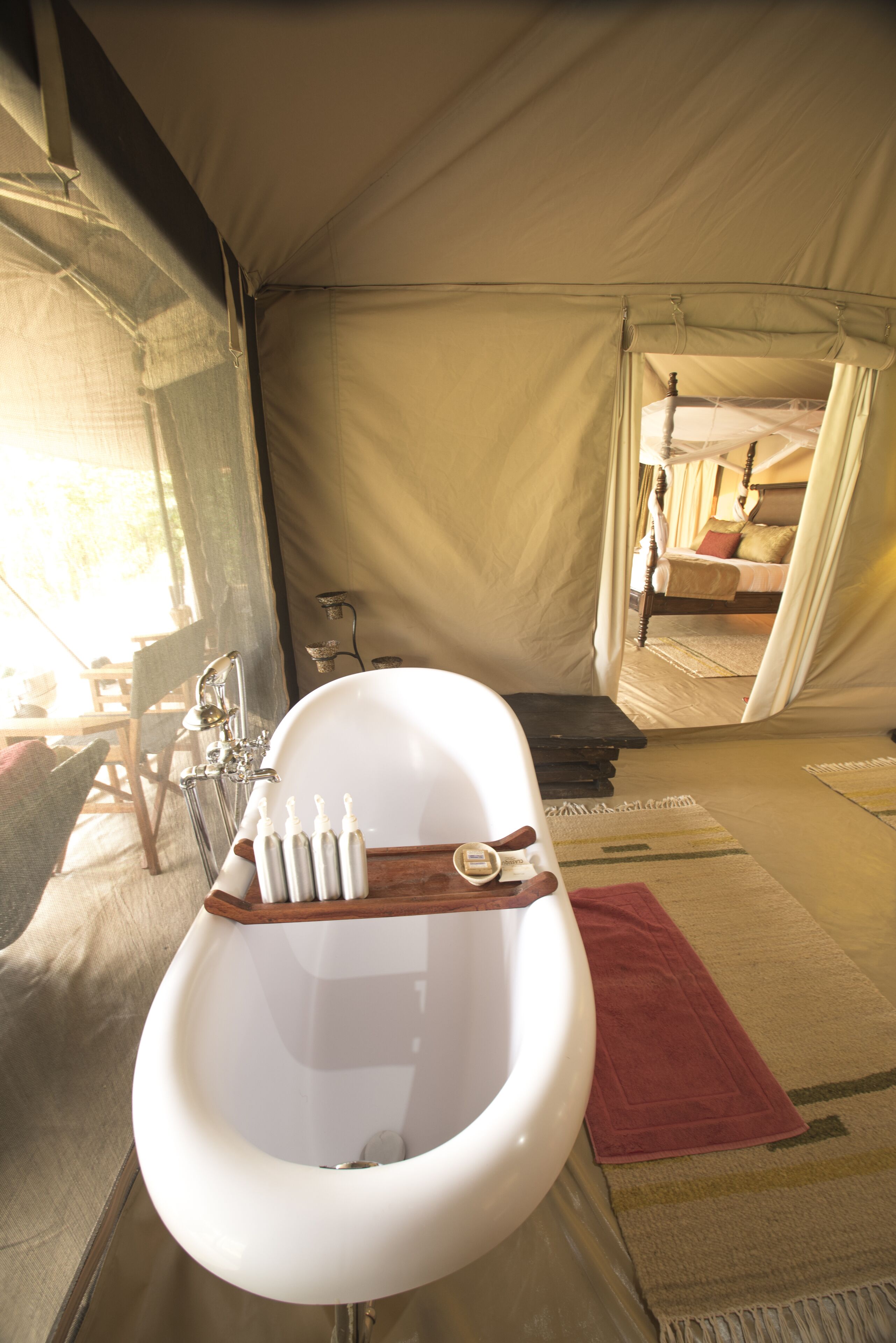 A tent with a white bathtub, a wooden bench, and a bed with a canopy.
