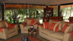 A tented room with two beige sofas, red-striped cushions, a small wooden table with wine glasses, and a view of trees outside.