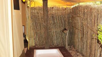 A small, enclosed shower area with a wooden post and a hanging light fixture.