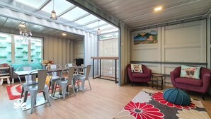 A modern living room with a dining area, featuring a large window, a hanging light fixture, and a colorful rug. - Arundina Cameron Highlands (Tanah Rata)