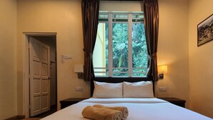 A hotel room with a bed, a window with curtains, a nightstand, a wall-mounted lamp, and a door. - Arundina Cameron Highlands (Tanah Rata)