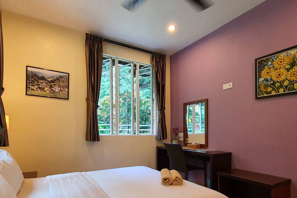 Quarto de hotel com uma cama, uma mesa e duas janelas com cortinas.