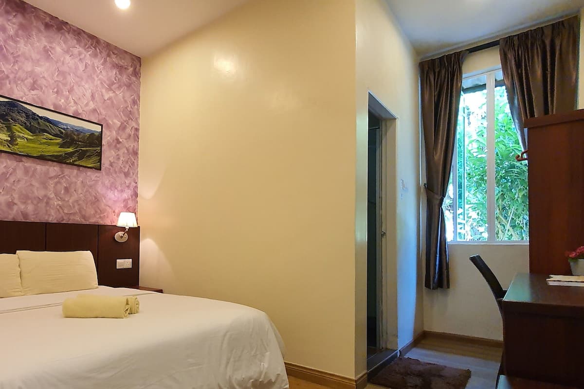 Quarto de hotel com cama, abajures, um quadro na parede e uma janela com cortinas.