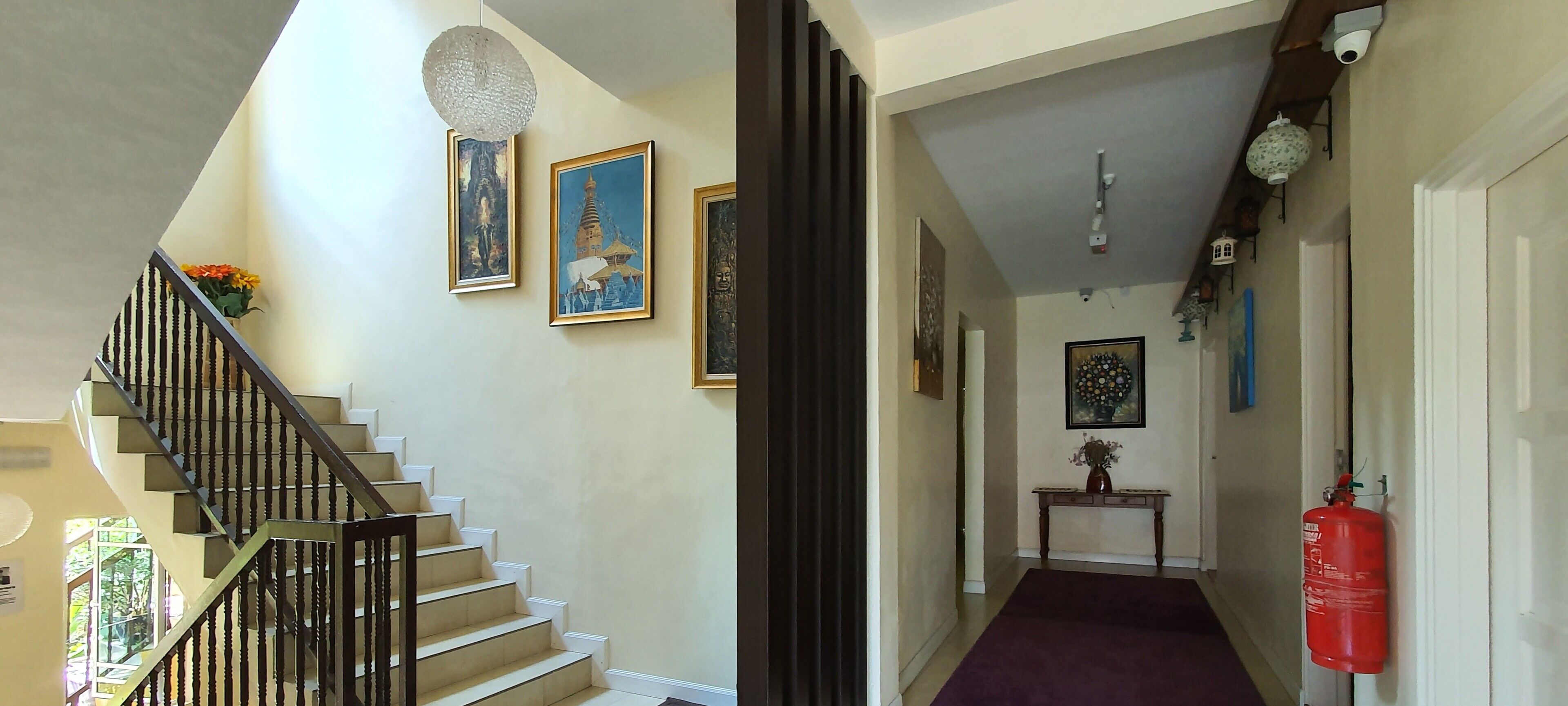 Un escalier avec une rampe noire menant à un palier orné de tableaux encadrés et d’un vase.