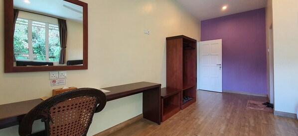 A hotel room with a wooden desk, a chair, a mirror, a wardrobe, and a door leading to another room.
