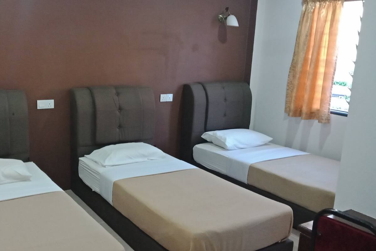 Ein Hotelzimmer mit drei Einzelbetten, jeweils mit Kopfstütze und weißer Bettwäsche.