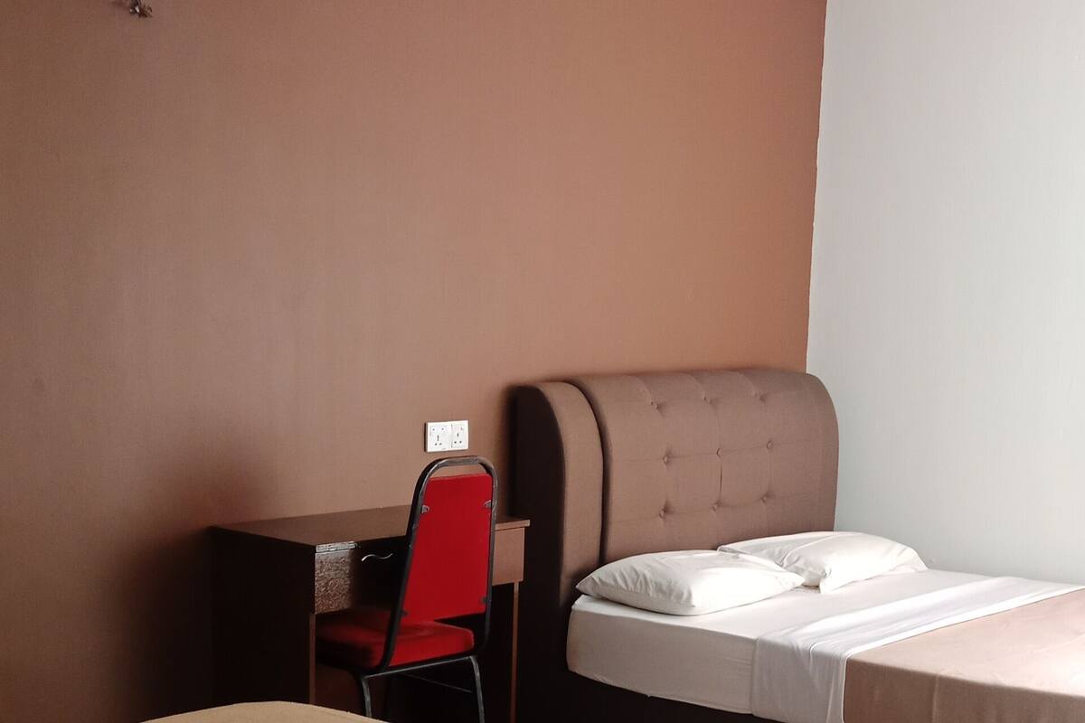 Ein Hotelzimmer mit zwei Einzelbetten, einem Schreibtisch mit Stuhl, einem Deckenventilator und einer Wandsteckdose.