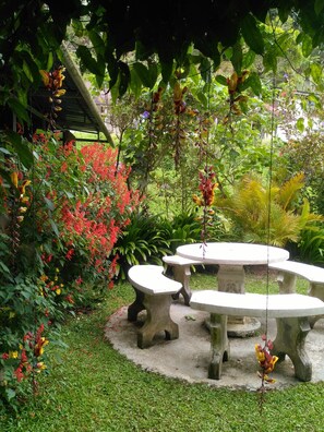 Un jardín con una mesa de piedra y bancos, rodeado de diversas plantas y flores.