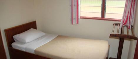A single bed with a wooden frame and white bedding, a window with curtains, and a wooden chair.