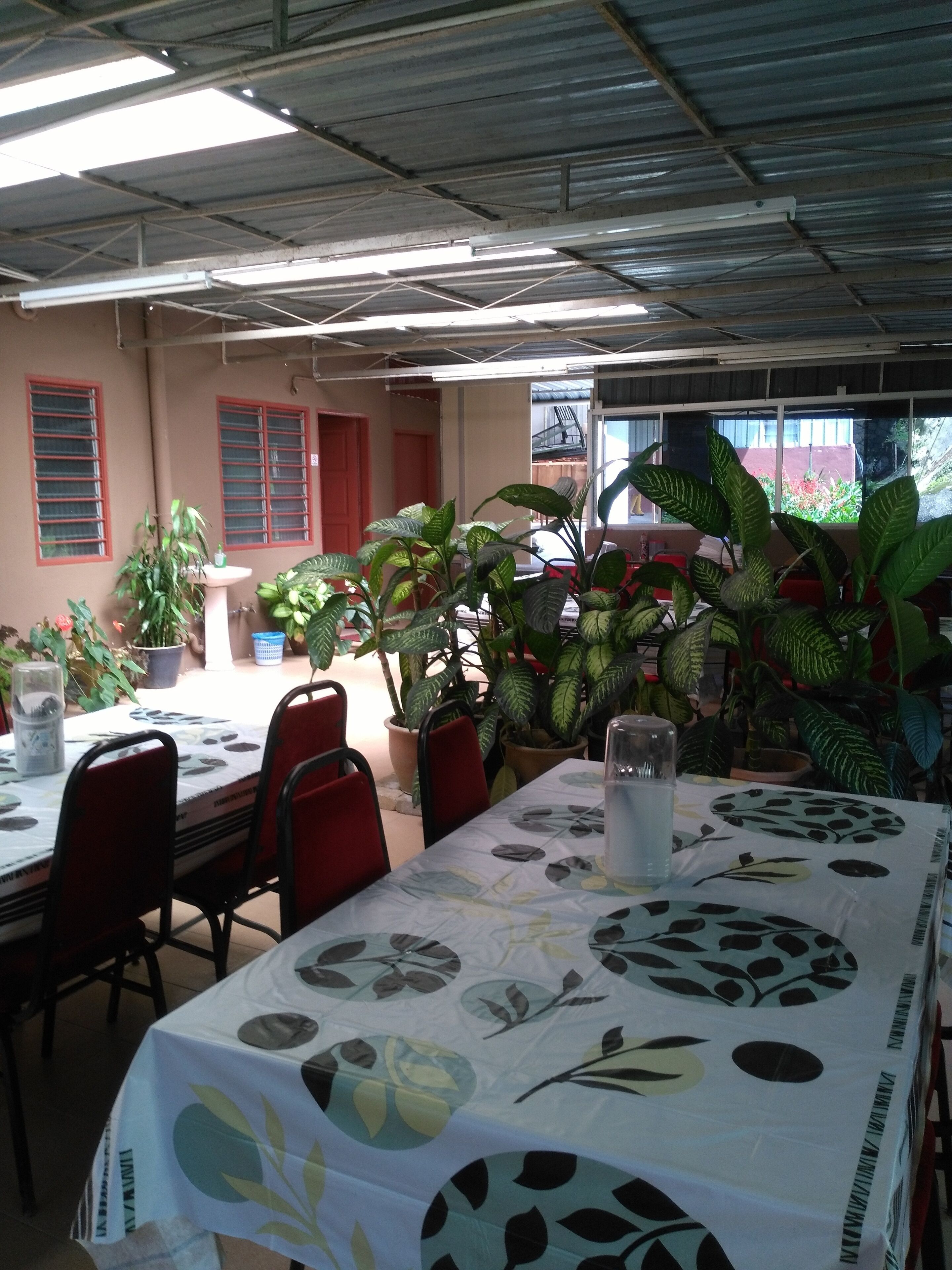 Zona pranzo con tavoli ricoperti da tovaglie a fantasia, circondata da piante in vaso.