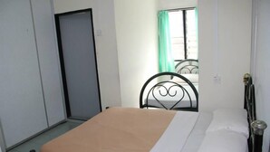 Una habitación pequeña y sencilla con una cama, una silla y un ventanal con cortinas.