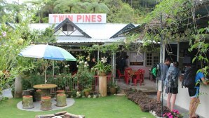 Un jardín con un letrero que dice "TWIN PINES", mobiliario exterior y una chimenea.