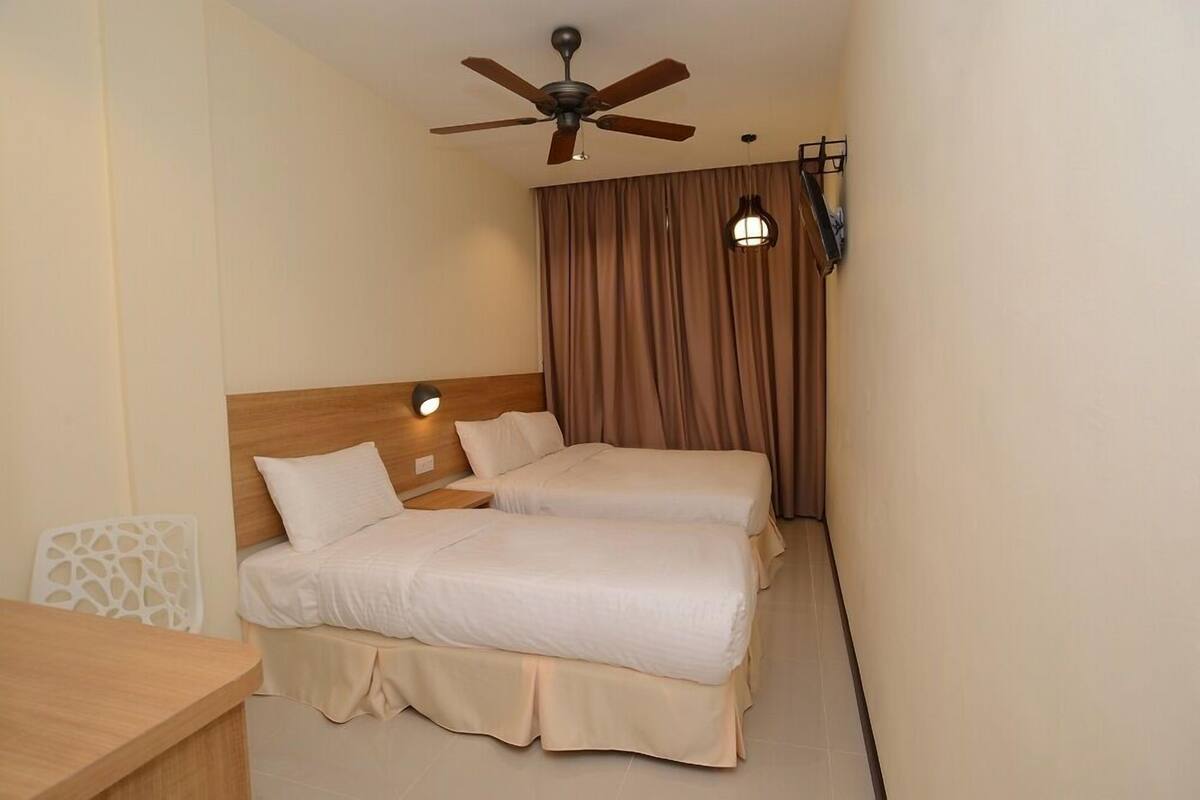 A hotel room with two beds, a ceiling fan, a nightstand, a table, and a curtain.