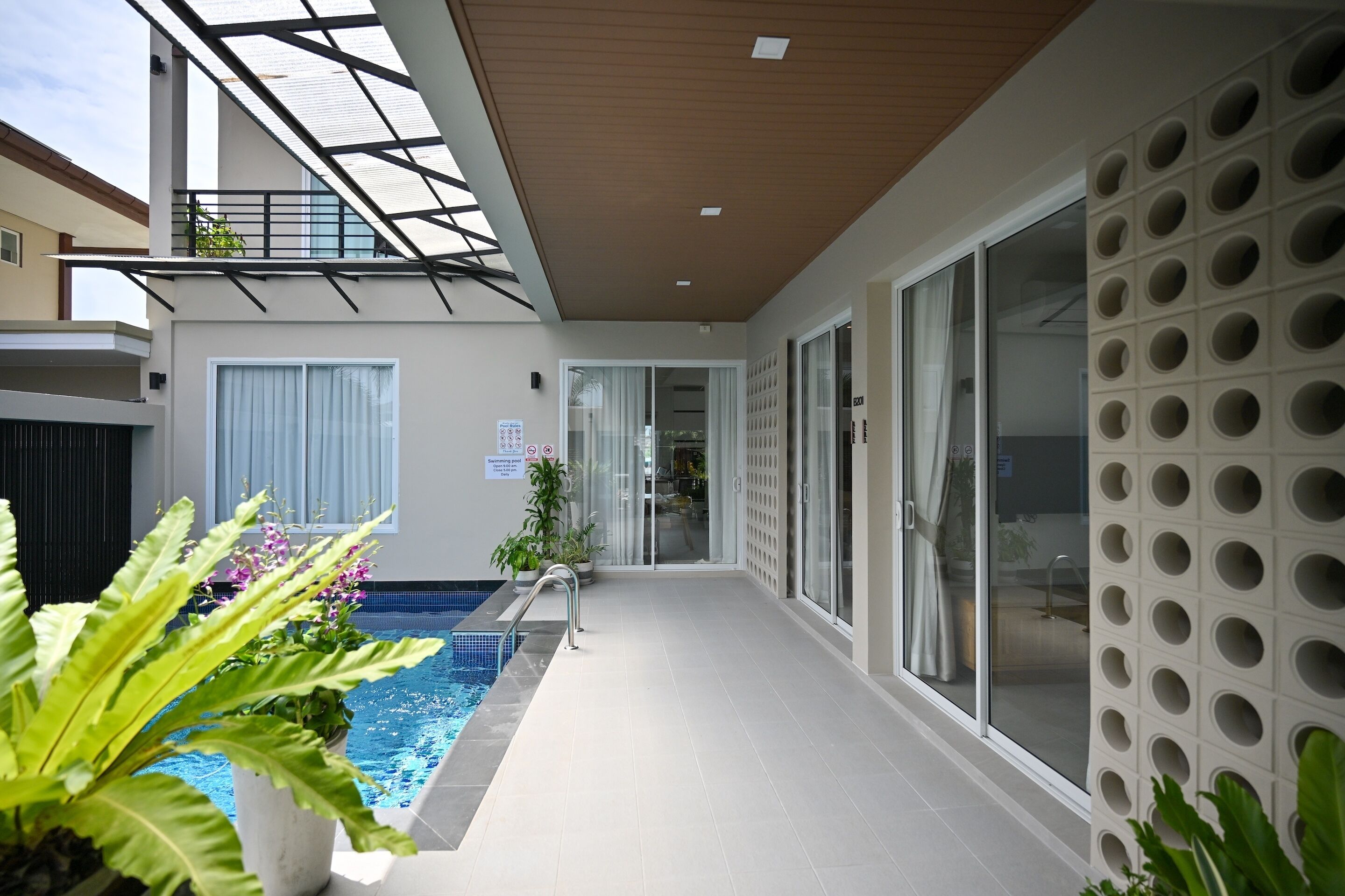 Un espace piscine intérieur moderne, doté d’un mur en verre, d’une piscine et de plantes en pot.