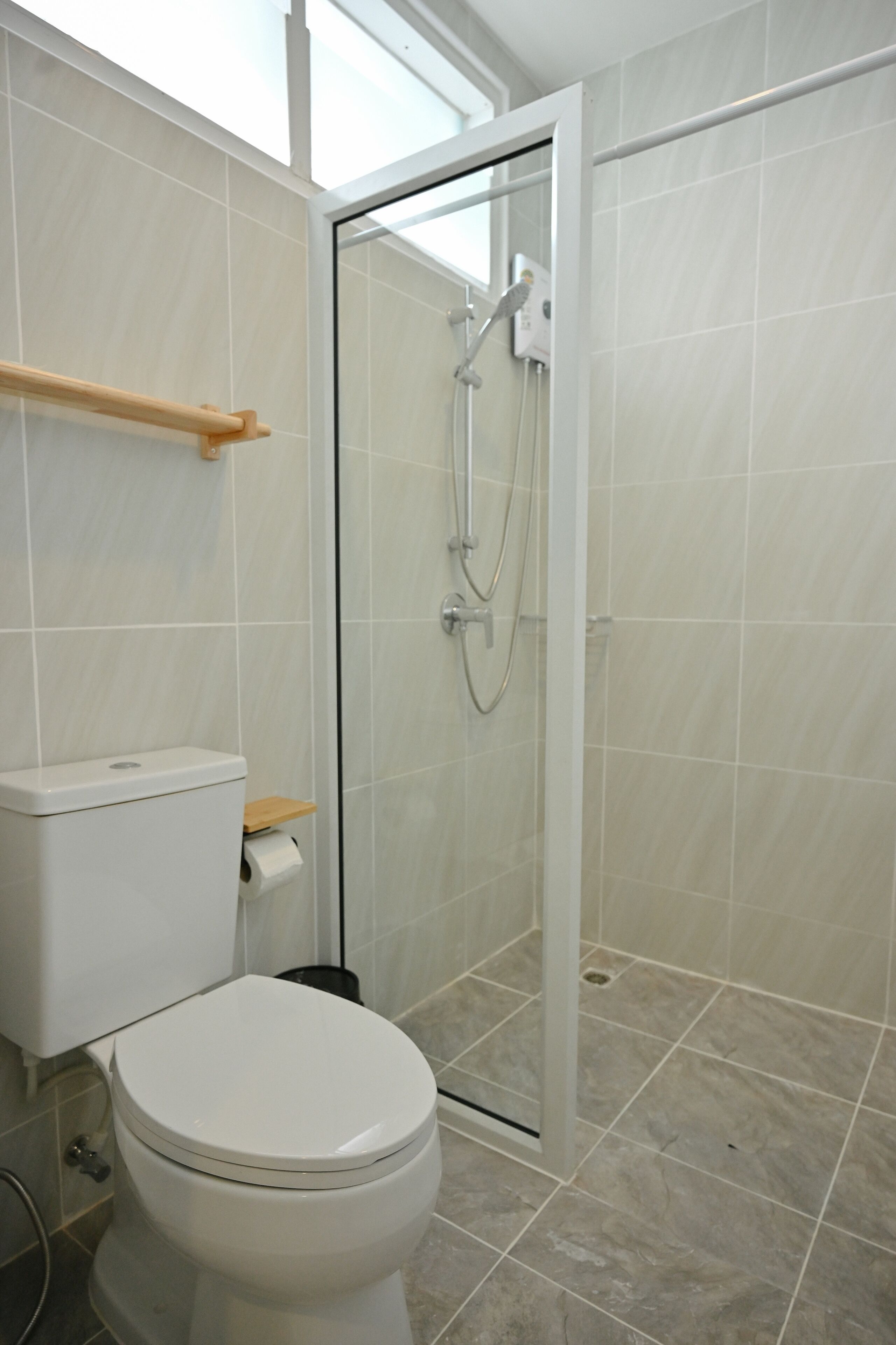 A bathroom with a toilet, a glass-enclosed shower, and a wooden shelf.