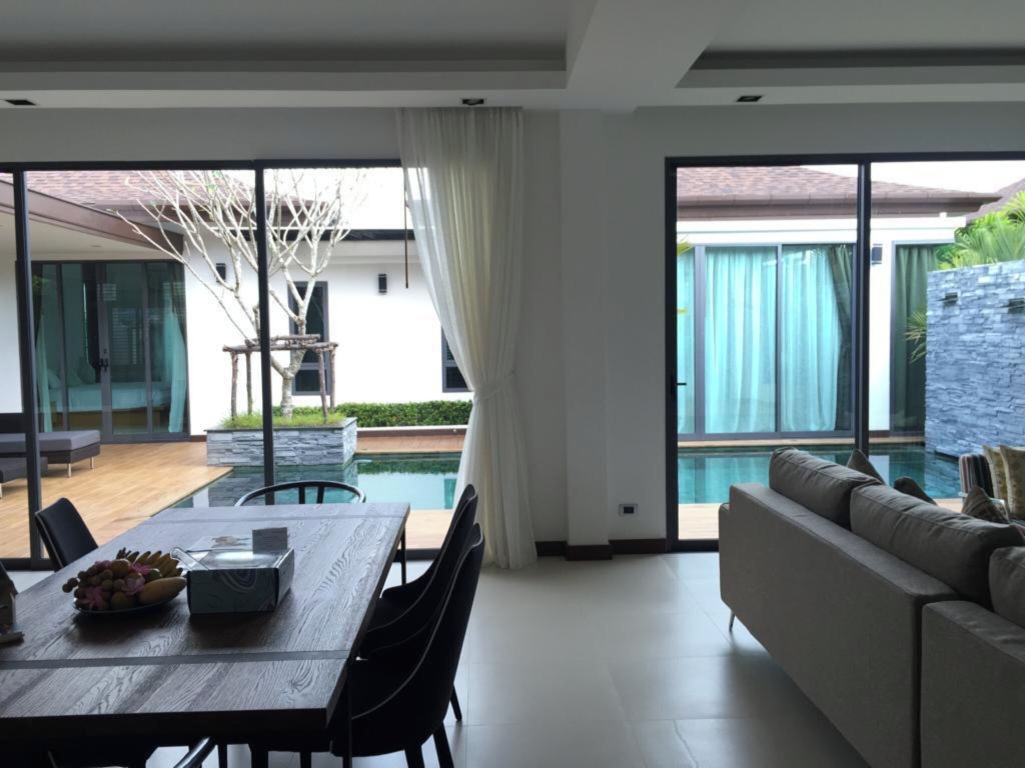 Una sala moderna con comedor, piscina y pared de piedra.