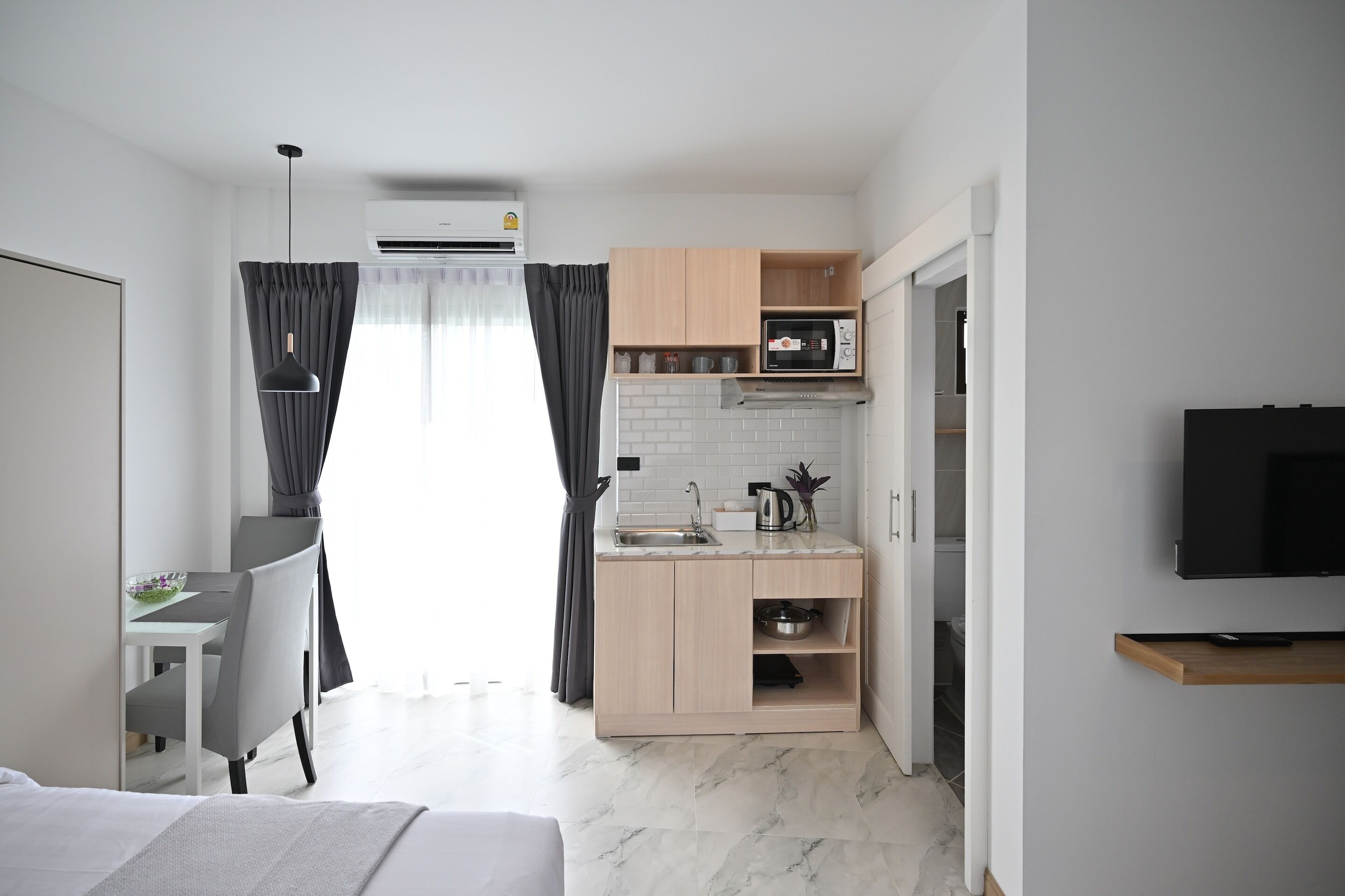 Kompakti hotellihuone, jossa on pieni keittiönurkkaus, sänky, televisio ja ikkuna, jossa on verhot.