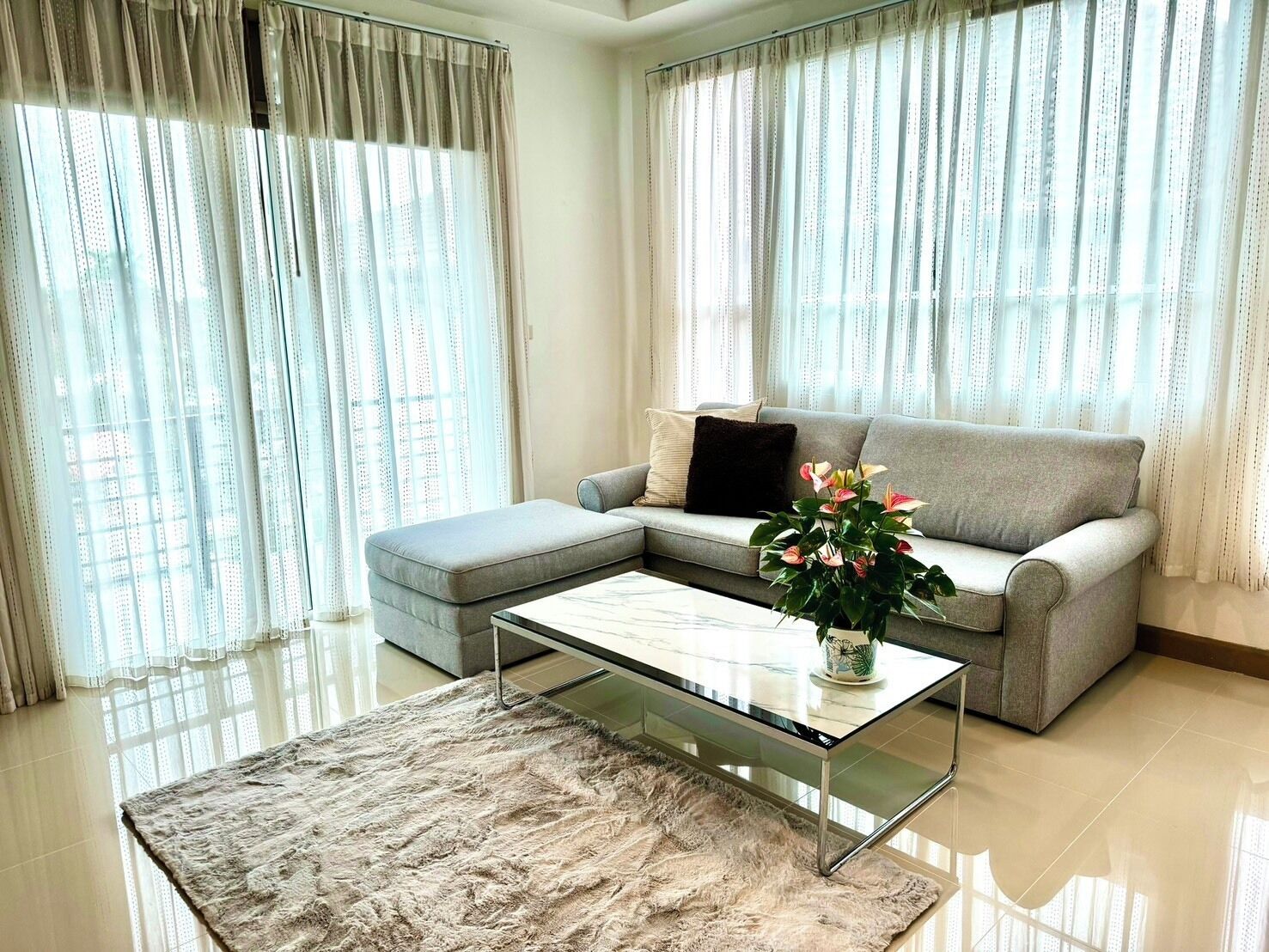 A modern living room with a grey sofa, a glass coffee table, and a fluffy rug.