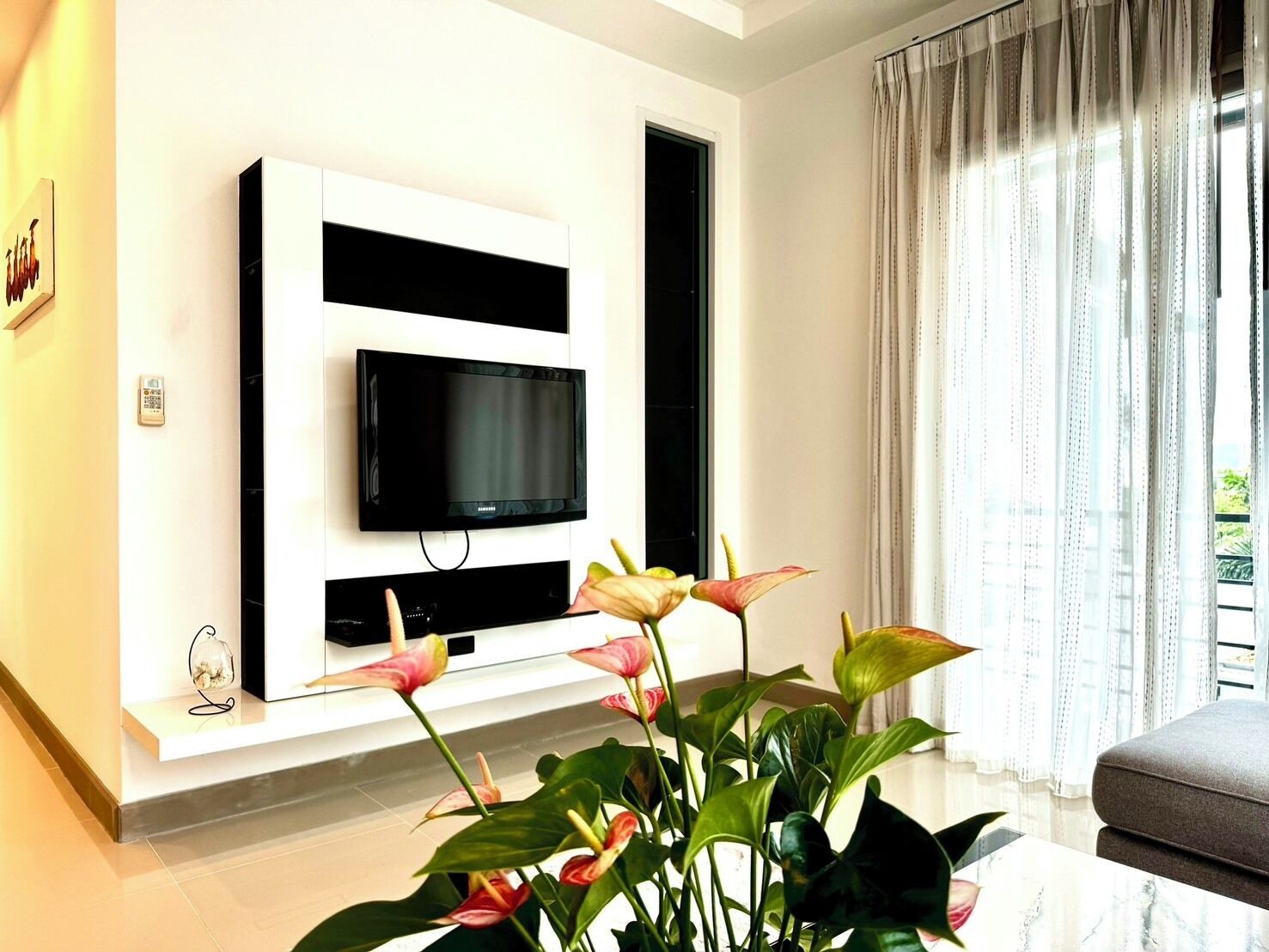 A modern living room with a mounted TV, a sofa, and a large window with curtains.