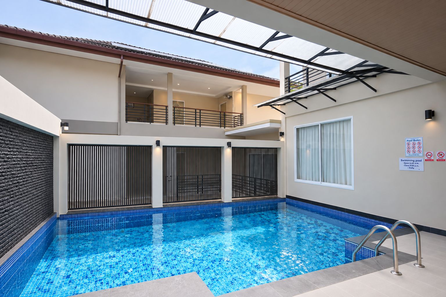 Une piscine dotée d’un toit en verre, offrant une vue sur l’étage supérieur, et un panneau indiquant les règles à respecter au bord de la piscine.