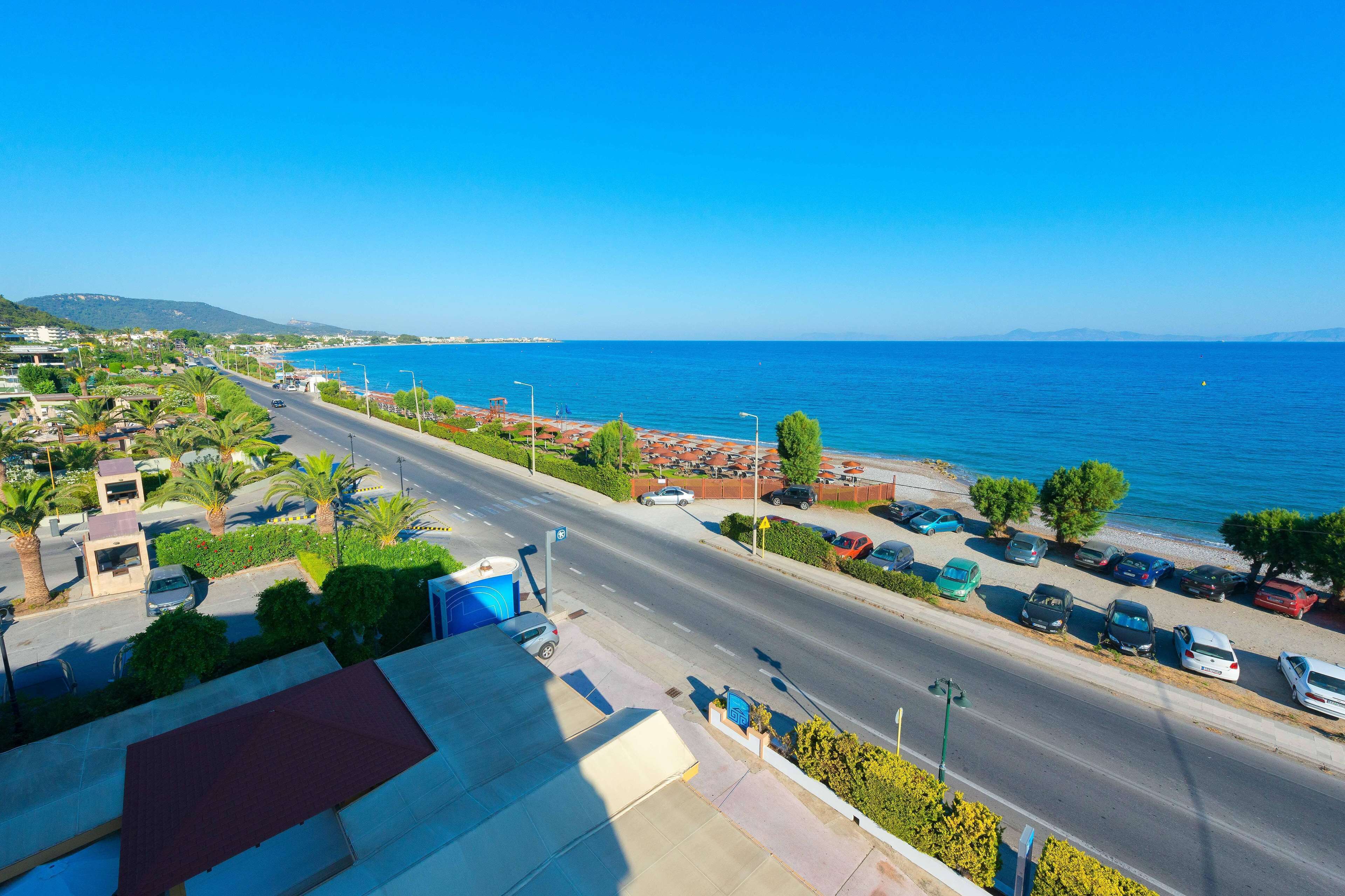 A coastal road with parked cars, a clear blue sky, and a view of the sea.
